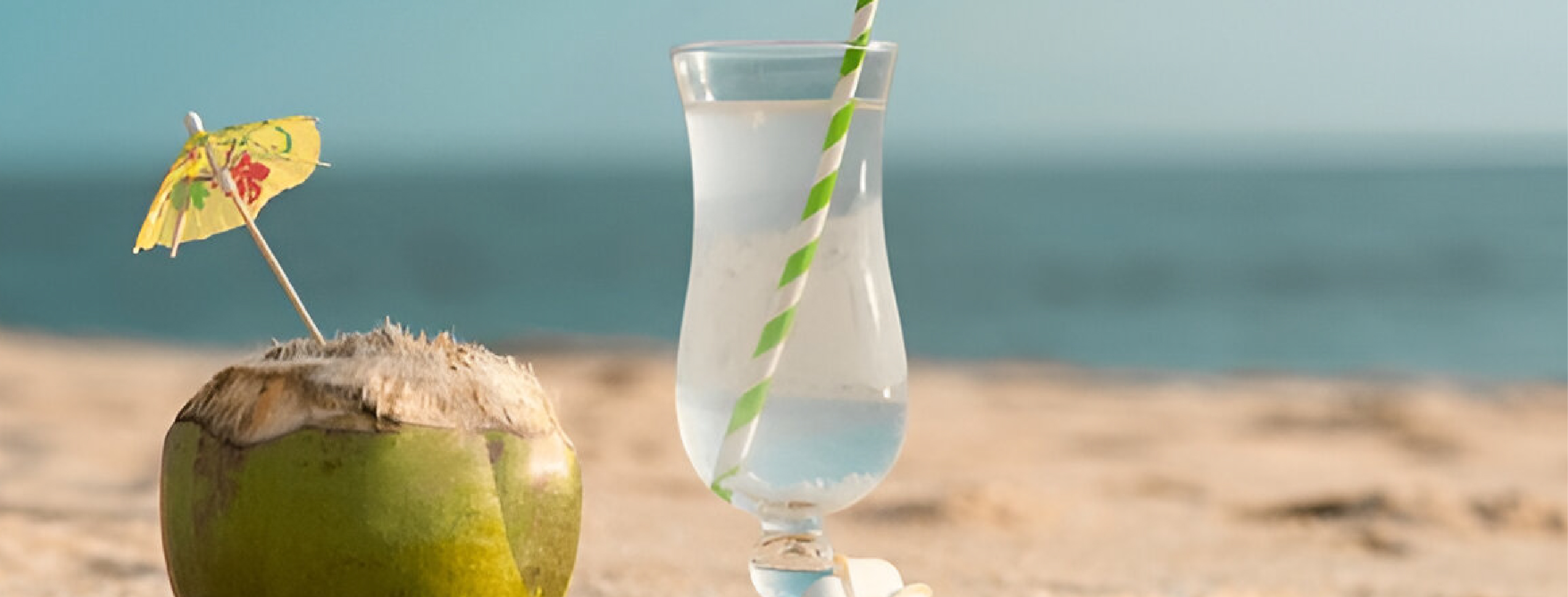 tender coconut and a glass of coconut water on sand