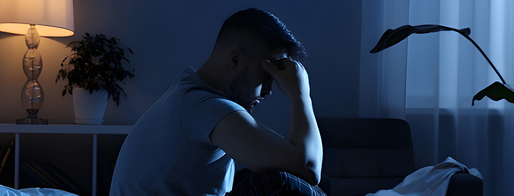 Man sitting on bed at night looking stressed or unable to sleep